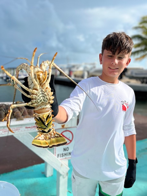 A Boy on a Boat Displaying a Caught Lobster at Sea Bird Marina